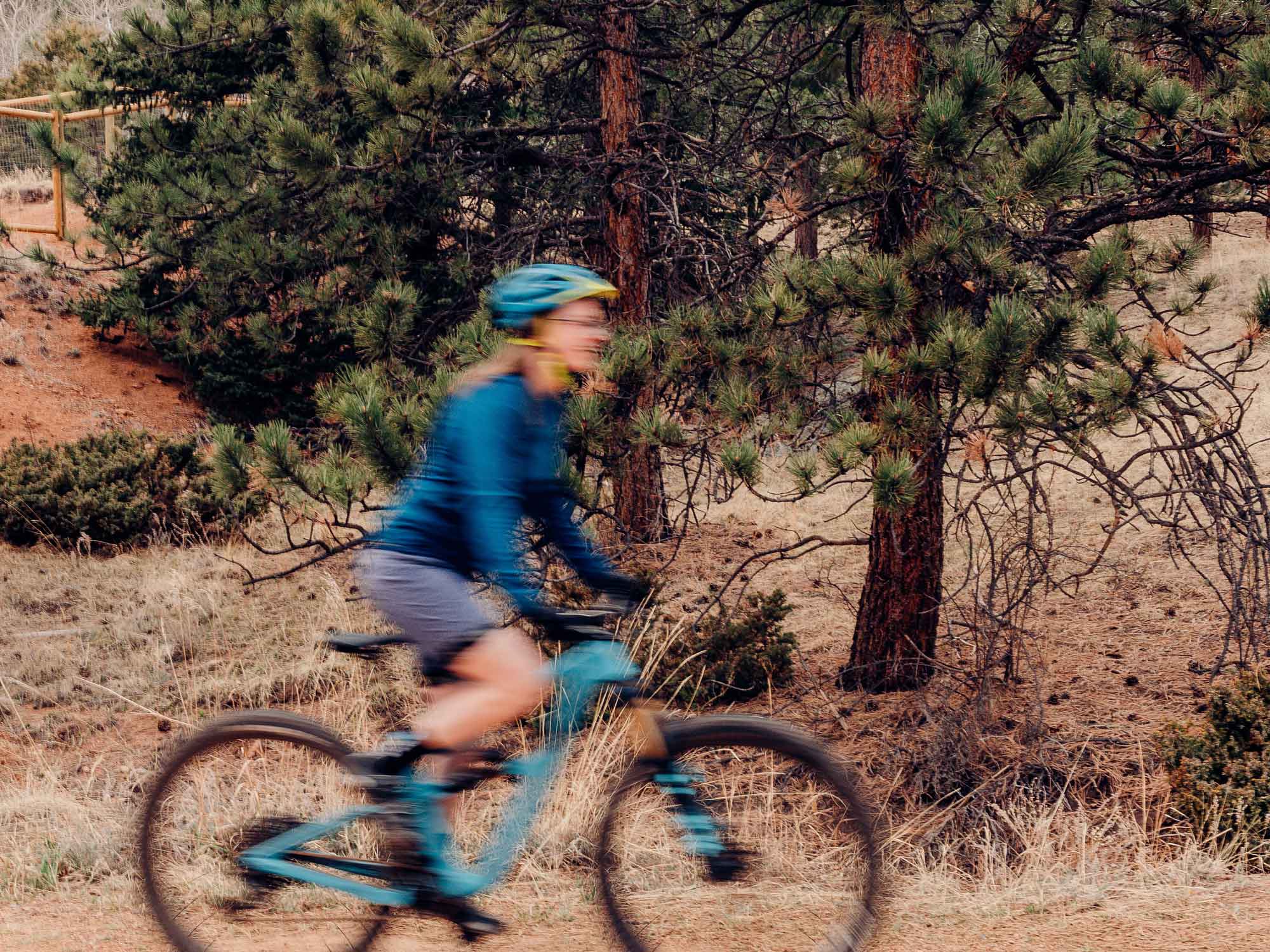 Me, Jacquelyn, riding my blue Ibis Ripmo on a dirt road with pine trees in the background